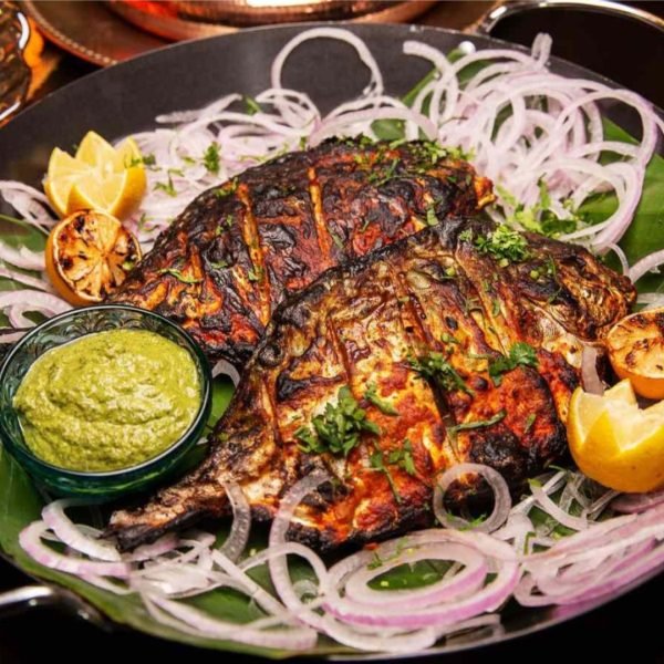 Whole Tandoori Pomfret grilled with Indian spices, garnished with lemon slices and herbs on a platter.
